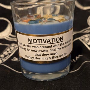 May include: A blue candle in a clear glass with the word "MOTIVATION" on a label. The label also includes text about the candle's purpose. The candle is decorated with colorful, small pieces.