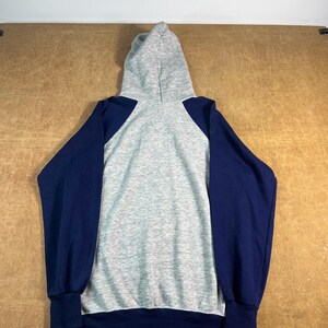 May include: A gray hooded sweatshirt with navy blue sleeves. The back of the hoodie is gray, with navy blue sleeves and cuffs. The hood is also gray. The sweatshirt is made of a soft, comfortable material.