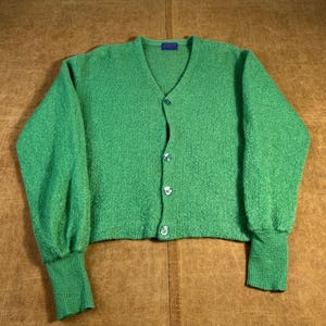 Op de afbeelding: Een felgroen vest met een V-hals en knoopsluiting. De trui heeft lange mouwen met geribde manchetten en een getextureerde gebreide stof. De knopen zijn transparant met een zilverkleurige rand. Het vest is een cropped model.