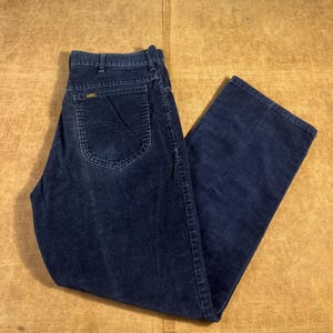 May include: Dark navy blue corduroy pants with a classic five-pocket design. The pants feature a straight leg cut and a visible Lee logo on the back pocket. The corduroy fabric has a ribbed texture.