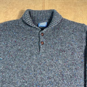 May include: A gray wool sweater with a shawl collar and three brown buttons. The sweater has a speckled pattern with flecks of blue, red, and green. A small blue tag is visible near the collar.