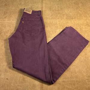 May include: A pair of purple denim jeans with a classic five-pocket design. The jeans feature a button and zipper closure, belt loops, and the Levi's brand patch on the back. The jeans are a solid color and appear to be unworn.