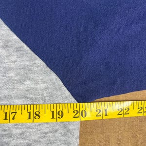 May include: Close-up of a blue and gray raglan sleeve shirt. A yellow measuring tape is laid across the shirt, showing measurements from 17 to 23 inches.