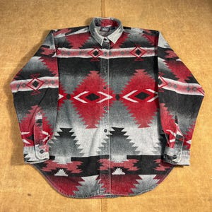 May include: A button-down shirt with a Southwestern-inspired pattern. The shirt features a gray, black, and red geometric design. The long-sleeved shirt has a collared neckline and buttoned cuffs.
