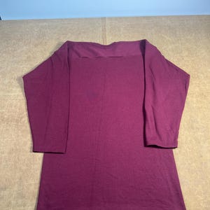 May include: A long-sleeved, burgundy-colored shirt with a boat neck. The shirt is made of a soft material and has a relaxed fit. The sleeves are three-quarter length.