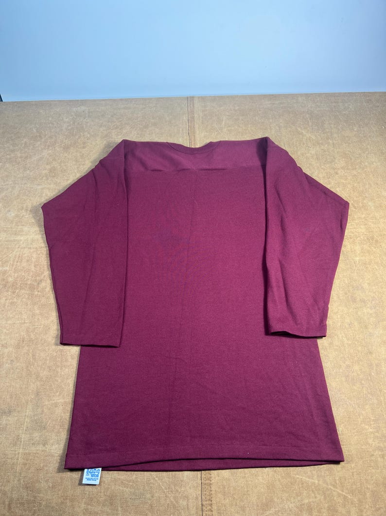 May include: A long-sleeved, burgundy-colored shirt with a boat neck. The shirt is made of a soft material and has a relaxed fit. The sleeves are three-quarter length.