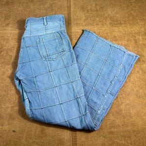 May include: Light blue denim trousers with a patchwork design. The trousers feature a high waist, pockets, and a wide leg. The denim is a light wash, and the patchwork creates a grid-like pattern across the fabric.