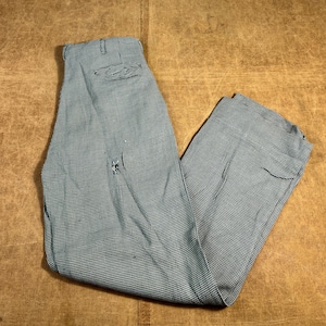 Puede incluir: Pantalones a cuadros azules y blancos. Los pantalones están doblados y reposan sobre una superficie marrón. Los pantalones tienen un pequeño agujero en la parte delantera. Los pantalones tienen cierre de botón y cremallera.