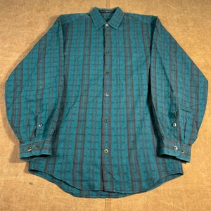May include: A long-sleeved button-down shirt in a teal and gray plaid pattern. The shirt has a classic collar, buttoned cuffs, and a chest pocket. The shirt is made of a woven fabric.