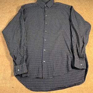 May include: A long-sleeved button-down shirt in a dark navy blue and tan plaid pattern. The shirt has a classic collar, buttoned cuffs, and a curved hem. The fabric appears to be a lightweight woven material.