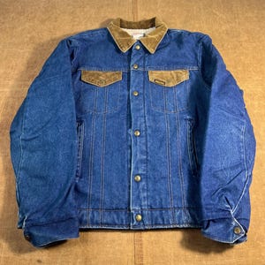 May include: Blue denim jacket with a brown corduroy collar and pocket flaps. The jacket has a button-up front, two chest pockets, and two side pockets. The jacket is lined with a soft, light-colored material.