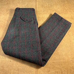 May include: Green and red plaid trousers. The pants are made of a textured fabric and feature a classic design with a buttoned back pocket. The plaid pattern is a combination of green and red lines, creating a traditional look.