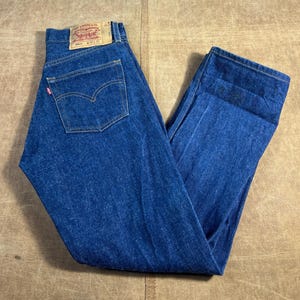May include: Classic blue denim jeans with a faded look. The jeans feature a traditional five-pocket design, a red tag on the back pocket, and a leather patch. The waist size is 30 inches and the inseam is 32 inches.
