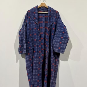 May include: A long, blue robe with a plaid pattern of red squares. The robe is hanging on a wooden hanger against a white wall. The robe has long sleeves and a collar.