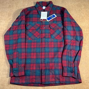 May include: A red and teal plaid flannel shirt with two chest pockets and button fastenings. The shirt has a collar and long sleeves with buttoned cuffs. A tag is attached to the shirt.