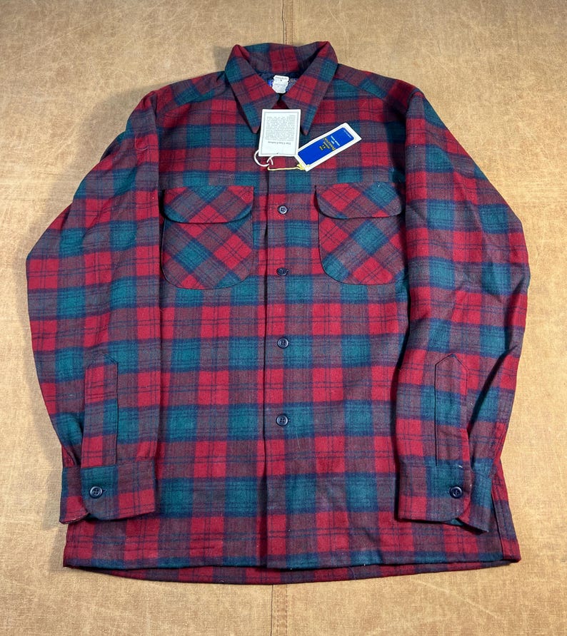 May include: A red and teal plaid flannel shirt with two chest pockets and button fastenings. The shirt has a collar and long sleeves with buttoned cuffs. A tag is attached to the shirt.