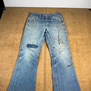 May include: A white ceramic mug with a black handle and the text "But First, Coffee" in a bold, black font. The mug is set against a blurred background, suggesting a cozy setting.