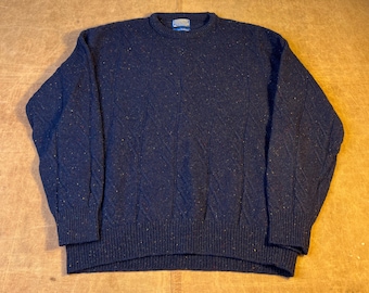 May include: A navy blue sweater with a textured diamond pattern. The sweater has a crew neck and ribbed cuffs and hem. The fabric has flecks of color throughout. A small tag is visible on the back of the neck.