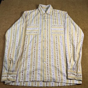 May include: A long-sleeved shirt with a vertical striped pattern in beige, white, and brown. The shirt features two chest pockets and buttoned cuffs. The design has a vintage aesthetic.