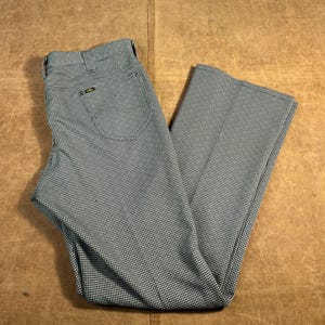 May include: A pair of vintage Lee pants in a houndstooth pattern. The pants are a mix of black and white, with a classic five-pocket design and a flared leg. The pants are made of a durable fabric and are likely from the 1970s.