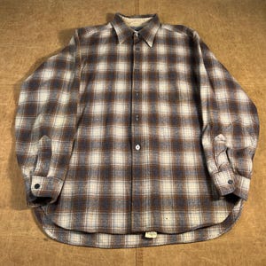 May include: A button-down shirt with a plaid design in brown, cream, and blue. The long-sleeved shirt features a collar, buttoned cuffs, and a curved hem. The fabric looks to be a soft, woven material, suitable for cooler weather.