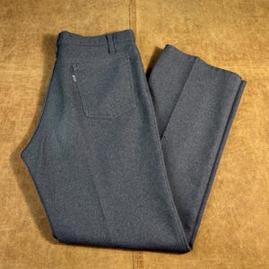 May include: A pair of gray trousers with a classic design. The pants feature a back pocket and a small tag. The fabric appears to be a medium-weight material, suitable for various occasions. The trousers are folded neatly.