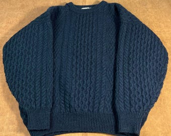 May include: A navy blue cable knit sweater with a crew neck. The sweater has a textured pattern on the sleeves and body, and ribbed cuffs and hem. This warm, cozy sweater is perfect for cold weather.