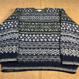 Peut inclure: Un pull à motifs bleu marine, vert olive et blanc. Le pull à col rond a des manches longues et un motif géométrique. Le motif comprend des losanges. La matière est épaisse et texturée.