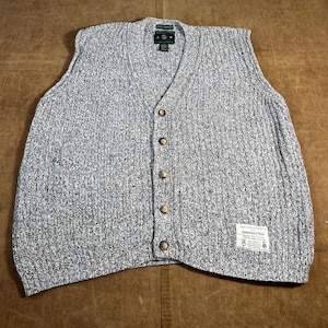 May include: A gray and white speckled knit vest with a V-neck and button-down front. The vest has a ribbed texture and a small label near the bottom. The buttons are a light brown color.