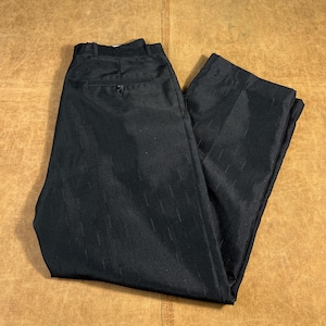 May include: Black dress pants with a subtle vertical stripe pattern. The pants are folded and laid flat on a brown surface. The pants have a button closure and pockets.