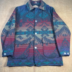 Peut inclure: Veste en laine à motifs dans les tons de bleu, rouge, vert et gris. La veste est dotée d'une fermeture boutonnée, de deux poches avant et d'un col. Le motif comprend des motifs géométriques et d'inspiration tribale.