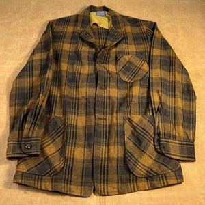 May include: A vintage plaid jacket in shades of gold and charcoal gray. The jacket features a classic collar, three front pockets, and button closures. The jacket's design includes a yellow lining and a single button on each cuff.