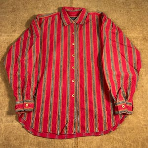 May include: A red button-down shirt with vertical stripes in yellow, navy, and white. The long-sleeved shirt has a classic collar and buttoned cuffs. The shirt is made of a lightweight fabric.