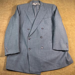 May include: A light blue double-breasted blazer with six buttons and notched lapels. The blazer has two rows of buttons and buttons on the sleeves. The fabric has a subtle texture.