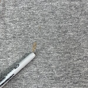 May include: Close-up of a gray, textured fabric with a white retractable pen. The pen has black text that reads "Sharpie FINE RETRACTABLE". There are brown stains on the fabric.