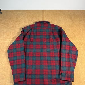May include: A red, green, and dark blue plaid flannel shirt. The shirt has long sleeves and a button-down front. The plaid pattern is a classic design, with a mix of red, green, and dark blue squares. The shirt is made of a soft, warm material.