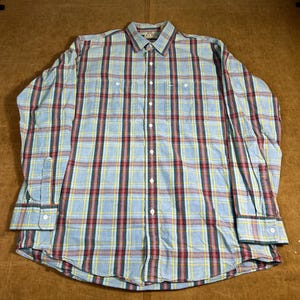 Może przedstawiać: Koszula z długim rękawem zapinana na guziki z wzorem w kratę w kolorze jasnoniebieskim, czerwonym, żółtym i ciemnozielonym. Koszula ma kołnierzyk zapinany na guziki, dwie kieszenie na piersi i mankiety zapinane na guziki. Koszula jest wykonana z tkaniny.