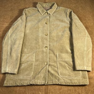 May include: Tan corduroy jacket with a collared neckline, button-down front, and two large front pockets. The jacket has a classic design and a soft, textured appearance. The interior collar lining features a plaid pattern.