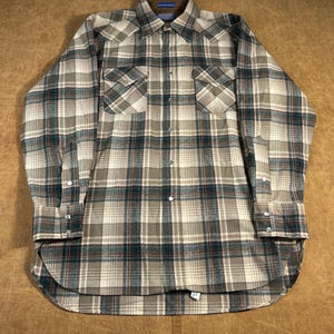 May include: A long-sleeved plaid shirt in shades of beige, brown, and teal. The shirt features two chest pockets, a button-down front, and buttoned cuffs. The collar is a darker brown color.