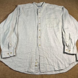 May include: A light gray long-sleeve shirt with a band collar and a single chest pocket. The shirt has a button-down front and buttoned cuffs. The fabric appears to be linen or a linen blend.