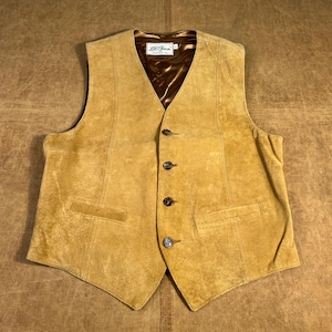 Puede incluir: Un chaleco de ante color canela con forro de satén marrón y cuatro botones oscuros. El chaleco tiene dos bolsillos delanteros y una etiqueta que dice "L.L. Bean". Un estilo clásico.