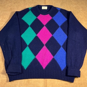 May include: A navy blue sweater with a colorful argyle pattern. The argyle design features green, pink, and blue diamonds. The sweater has a crew neck and ribbed cuffs and hem.