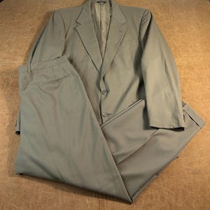 May include: A solid taupe suit consisting of a two-button blazer with notched lapels and matching trousers. The blazer features long sleeves, a chest pocket, and two front flap pockets. The trousers have a waistband with belt loops and side pockets.