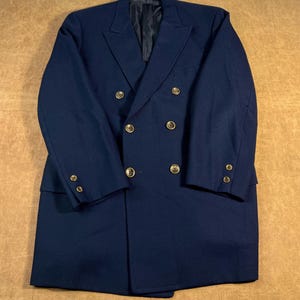 May include: A navy blue double-breasted coat with gold-colored buttons. The coat has a classic design with a notched lapel and a tailored fit. The buttons are evenly spaced and add a touch of elegance to the coat.