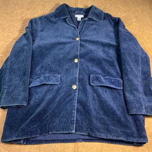 May include: A navy blue corduroy blazer with a collared neckline and three gold-colored buttons. The jacket has two front pockets and a button closure. The corduroy fabric has vertical ridges.