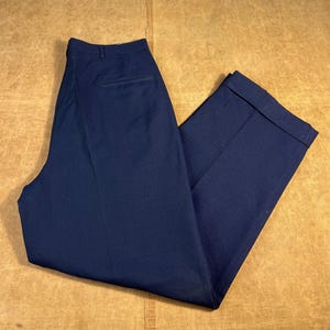 May include: Navy blue trousers with a classic design. The pants have a tailored fit, a button and zip closure, and a back pocket. The cuffs are neatly folded. The fabric has a subtle texture.