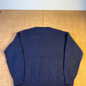 May include: A navy blue sweater with a textured diamond pattern. The sweater has a crew neck and ribbed cuffs and hem. The fabric has flecks of other colors throughout.