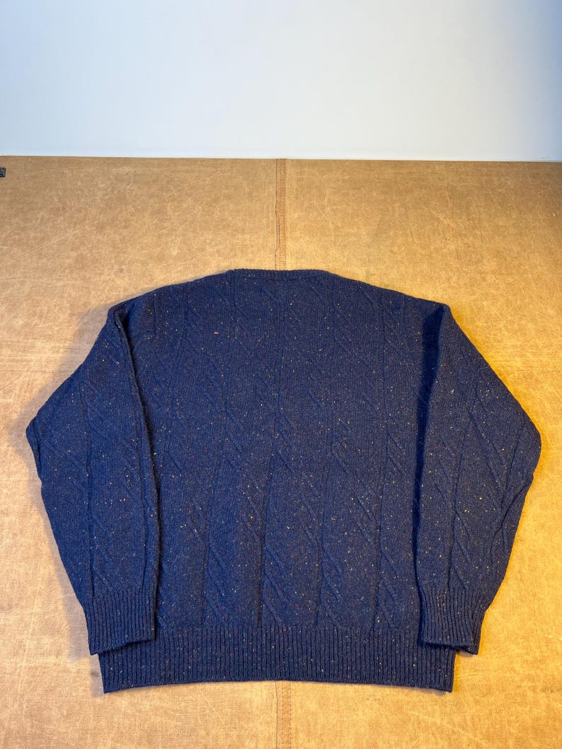 May include: A navy blue sweater with a textured diamond pattern. The sweater has a crew neck and ribbed cuffs and hem. The fabric has flecks of other colors throughout.