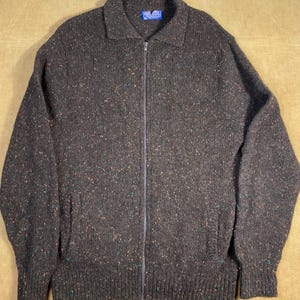 May include: A brown speckled zip-up cardigan sweater with a collared neckline. The sweater has two pockets on the front.