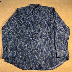 May include: A long-sleeved shirt with a distinctive pattern. The shirt has a repeating design of blue, grey, and black lines. It features a classic collar and buttoned cuffs. The fabric appears to be a lightweight material, suitable for warmer weather.